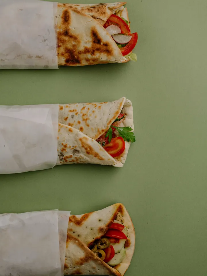 Tre manoucé arrotolate nella carta su fondo verde salvia, con pomodoro, ravanelli e prezzemolo